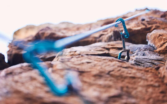 Rock climbing, mountain and closeup of rope and hook for adventure, freedom and extreme sports in nature. Fitness, hiking and carabiner, equipment or gear in stone for training, activity or challenge