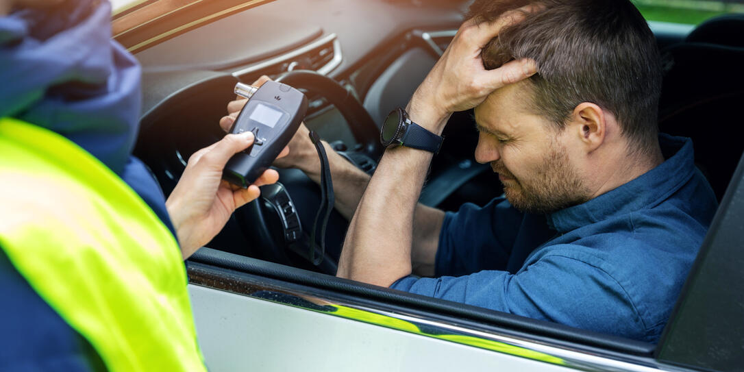 drink and drive concept - sad drunk man sitting in the car after police alcohol test with alcometer
