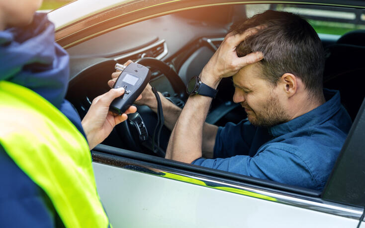 drink and drive concept - sad drunk man sitting in the car after police alcohol test with alcometer