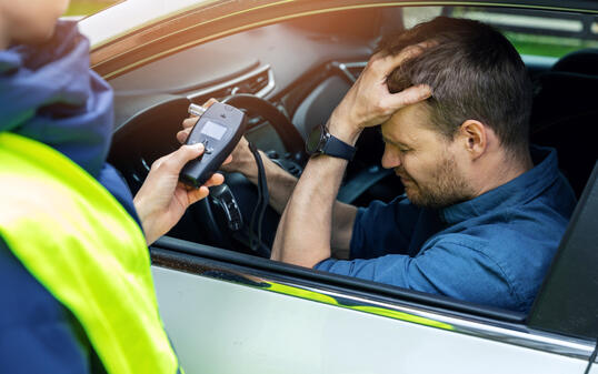 drink and drive concept - sad drunk man sitting in the car after police alcohol test with alcometer