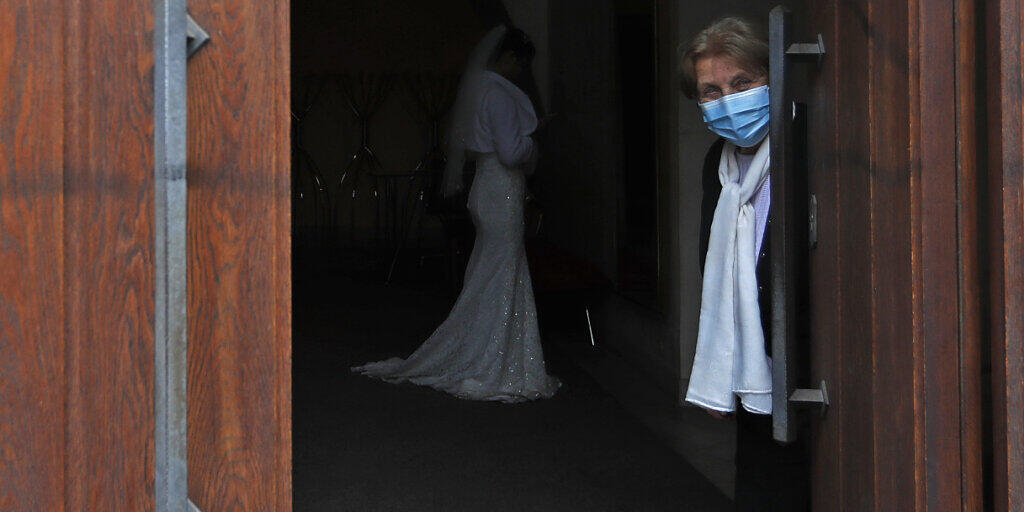 Eine Frau, die eine Mund-Nasen-Bedeckung trägt, hält eine Tür für eine Hochzeit in Prag geöffnet. Foto: Petr David Josek/AP/dpa Eine Frau, die eine Mund-Nasen-Bedeckung trägt, hält eine Tür für eine Hochzeit in Prag geöffnet. Foto: Petr David Josek/AP/dpa