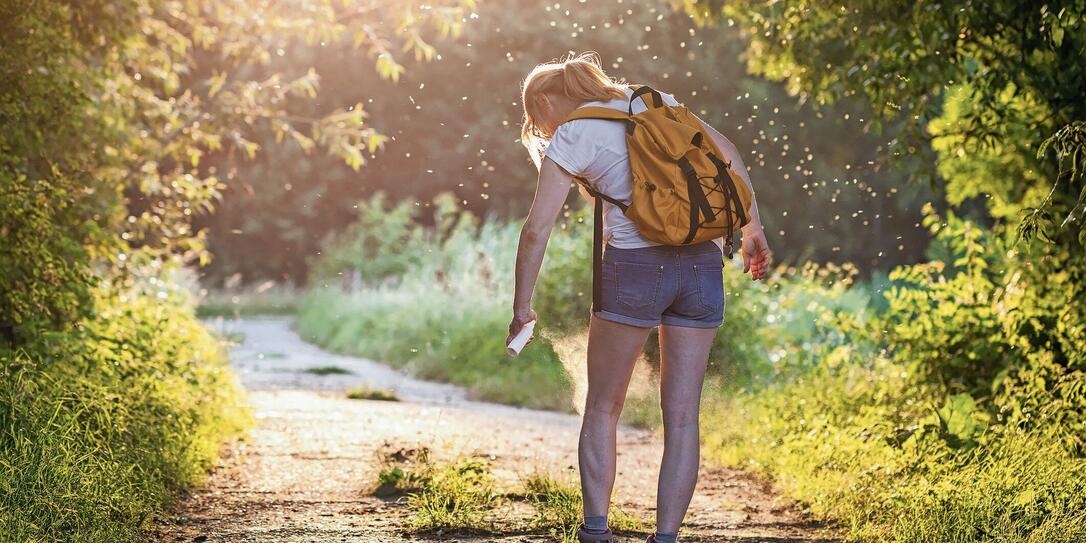 Woman with backpack applying insect repellent agains mosquito and tick outdoors