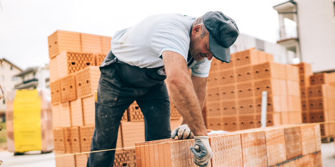 industrial worker building exterior walls, using hammer for laying bricks in cement. Detail of worker with tools and concrete