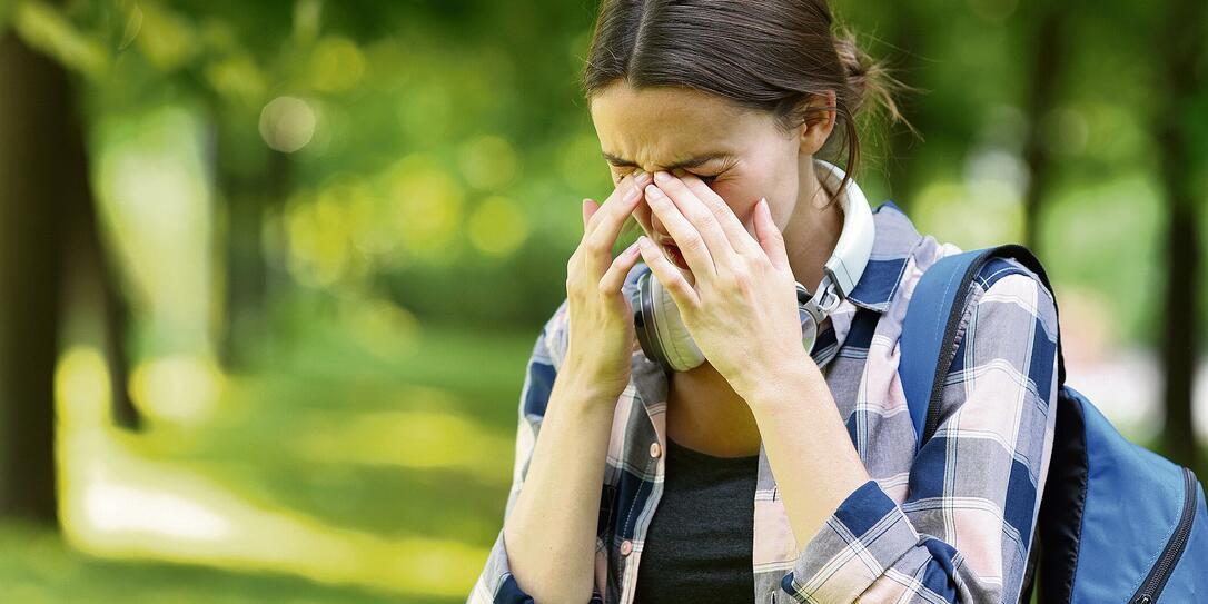 Student suffering allergy symptoms scratching eyes in a park Student suffering allergy symptoms scratching eyes in a park