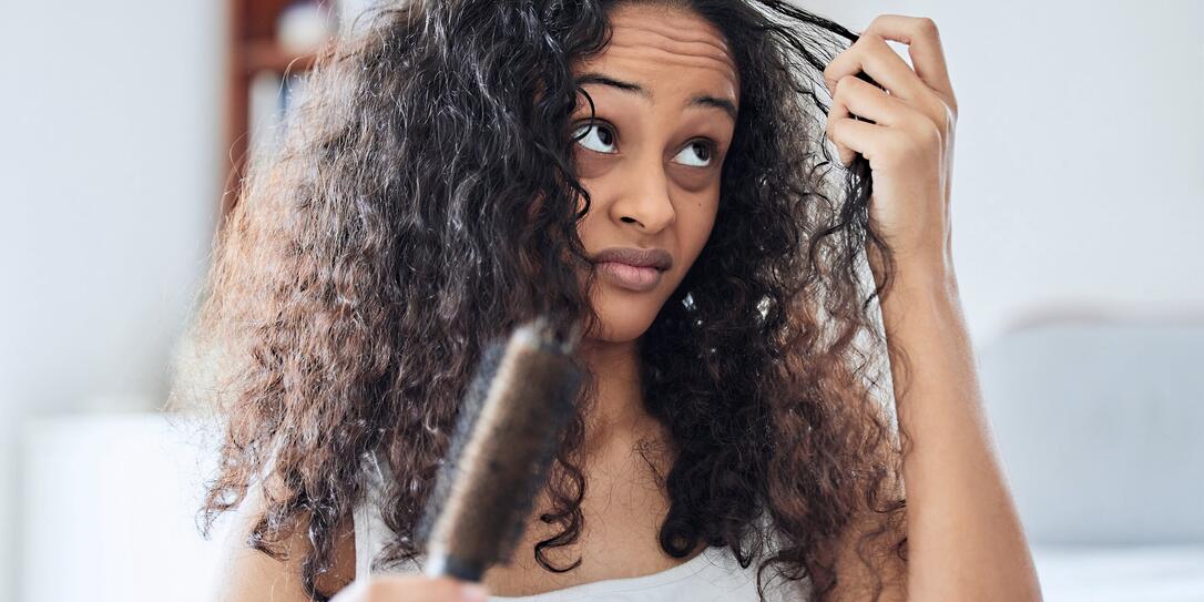 Shot of an attractive young woman standing alone at home and brushing her curly hair in the morning
