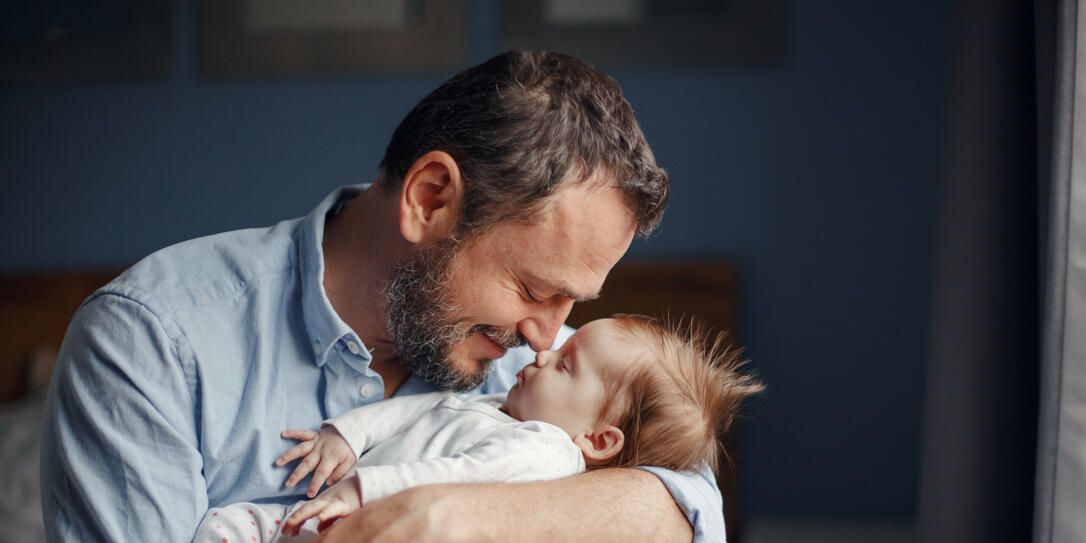 Middle age Caucasian father kissing sleeping newborn baby girl. Parent holding rocking child daughter son in hands. Authentic lifestyle parenting fatherhood moments. Single dad family home life.