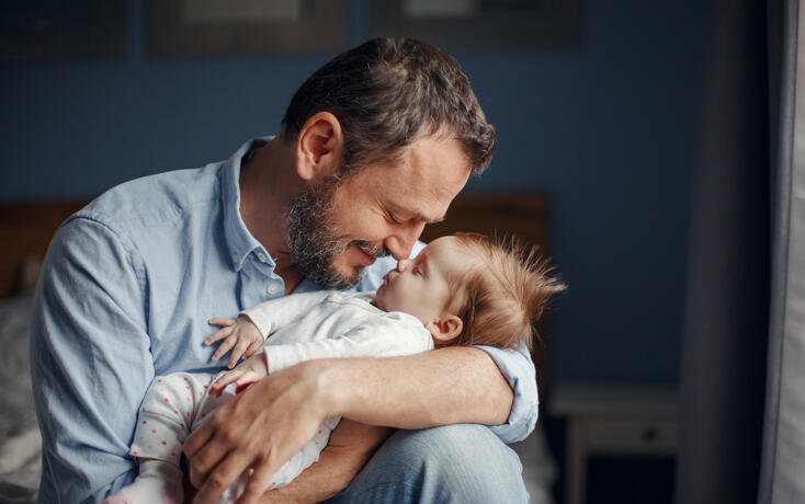 Middle age Caucasian father kissing sleeping newborn baby girl. Parent holding rocking child daughter son in hands. Authentic lifestyle parenting fatherhood moments. Single dad family home life.