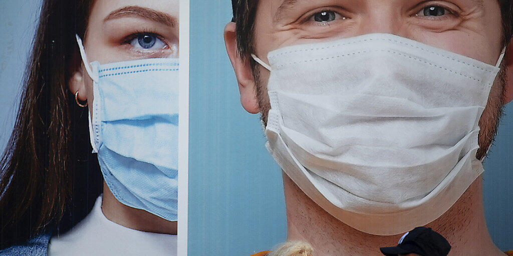 Passanten mit Schutzmasken gehen in Ramat Gan an einer Werbetafel vorbei, die das Tragen von Masken und die Einhaltung der Hygieneregeln während der Corona-Pandemie bewirbt. Foto: Oded Balilty/AP/dpa
