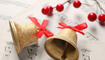 Golden shiny bells with red bows and decorative berries on music sheets, closeup. Christmas decoration