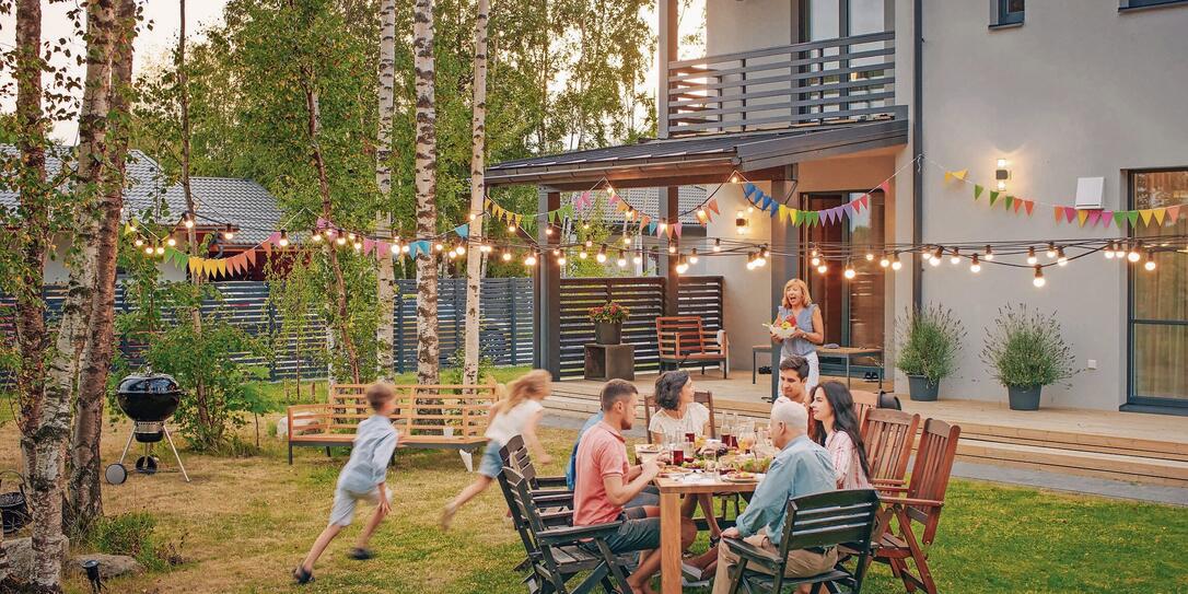Big Family Garden Party Celebration, Gathered Together at the Table Family, Friends and Children. People are Drinking, Passing Dishes, Joking and Having Fun. Kids Run Around Table.