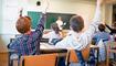 Schoolchildren at classroom with raised hands answering teacher's question.