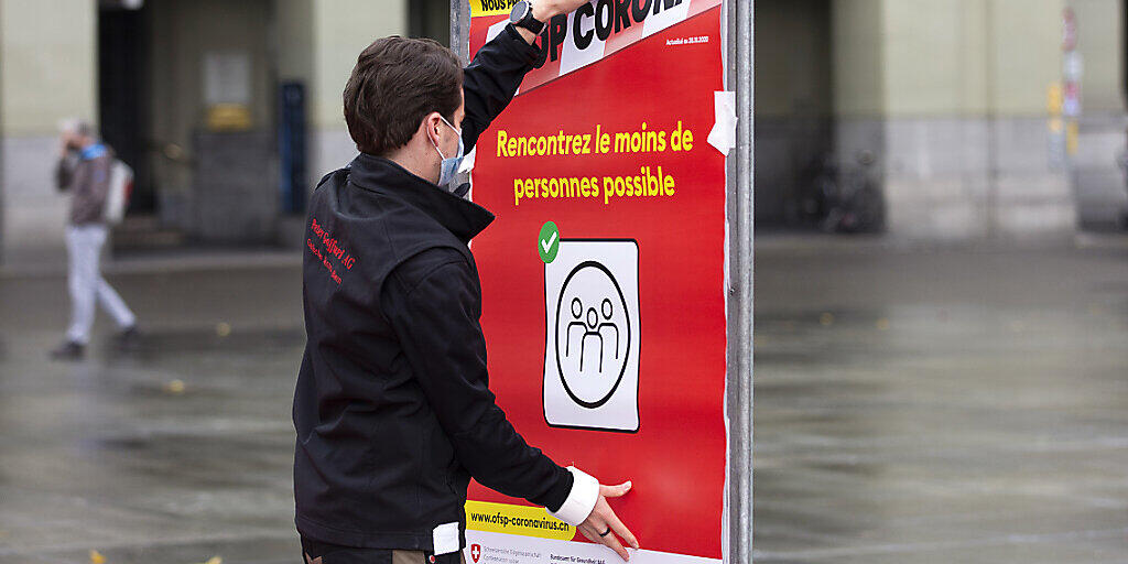 Coronavirus: Ein neues rotes BAG-Plakat mit der Verhaltensregel "Treffen Sie so wenige Menschen wie möglich"wird auf dem Bundesplatz in Bern installiert.
