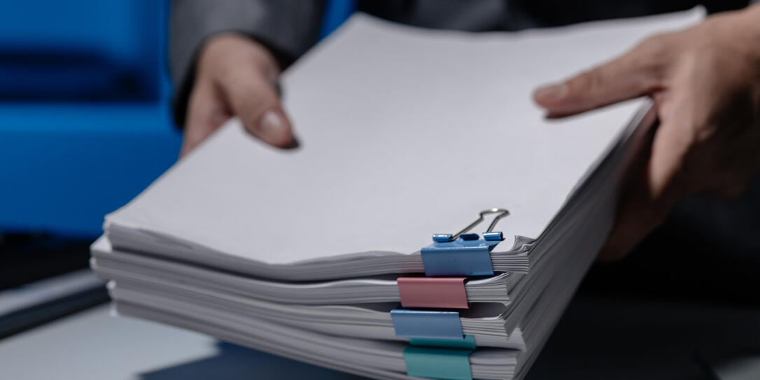 An employee was tidying up a pile of documents piled on his desk before returning home from work, A businessman is tidying up his desk because there are many documents he has completed.