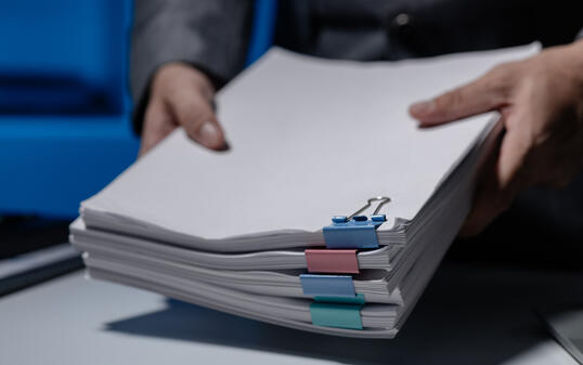 An employee was tidying up a pile of documents piled on his desk before returning home from work, A businessman is tidying up his desk because there are many documents he has completed.