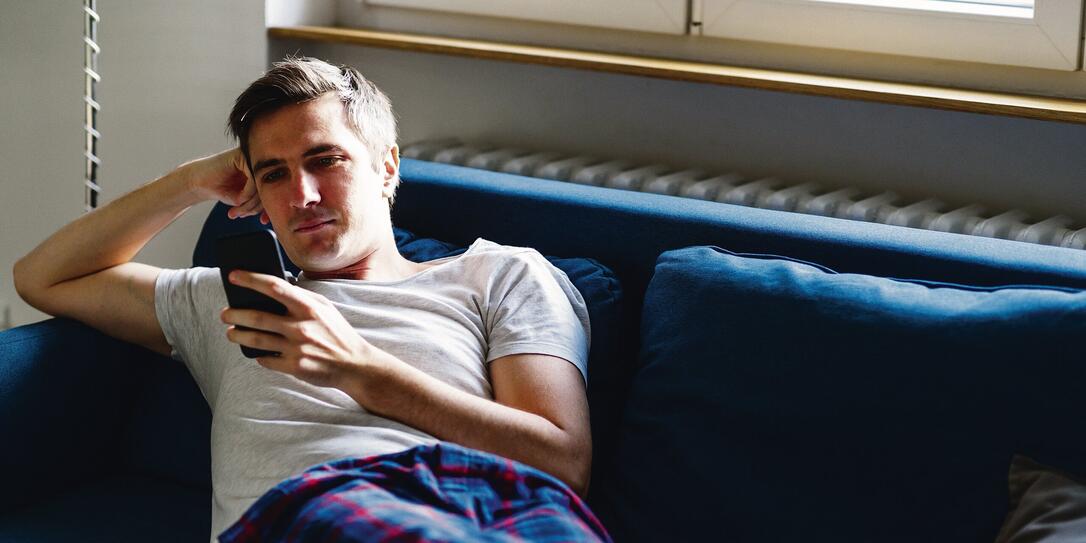 Young man on the sofa in pajamas checking smart phone Young man on the sofa in pajamas checking smart phone
