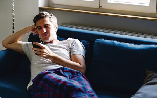 Young man on the sofa in pajamas checking smart phone