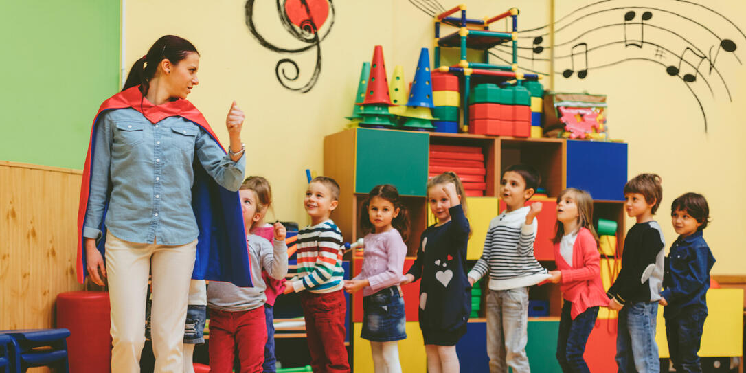 Group of children playing with their teacher in kindergarten