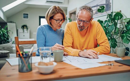 Senior couple sitting at table and looking into blueprints of their new home
