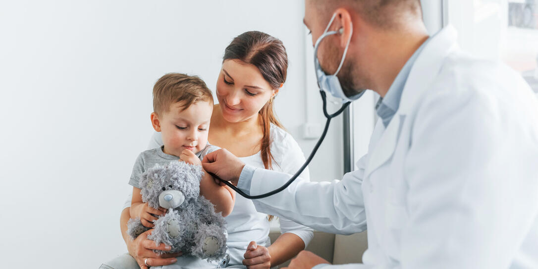 The little boy is being examined. Two doctors in white coats is in the clinic working together