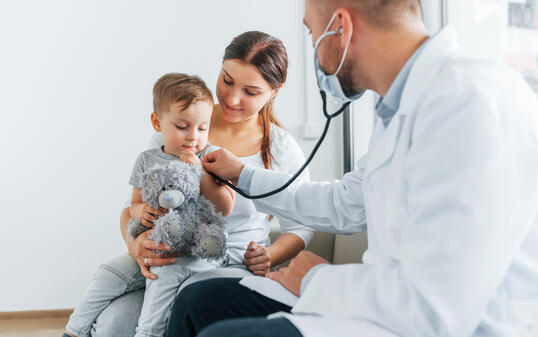 The little boy is being examined. Two doctors in white coats is in the clinic working together
