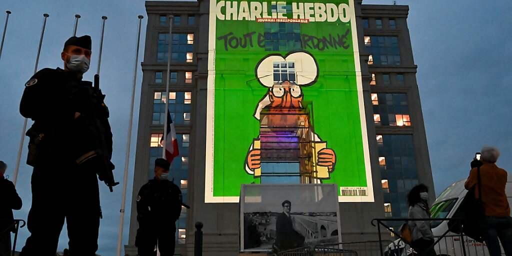 Polizeibeamte stehen Wache, während bei einer landesweiten Gedenkveranstaltung an den ermordeten Lehrer Samuel Paty Karikaturen der französischen Satirezeitung Charlie Hebdo auf die Fassade des Hotel de Region in Montpellier projiziert werden. Foto: Pascal Guyot/AFP/dpa Polizeibeamte stehen Wache, während bei einer landesweiten Gedenkveranstaltung an den ermordeten Lehrer Samuel Paty Karikaturen der französischen Satirezeitung Charlie Hebdo auf die Fassade des Hotel de Region in Montpellier projiziert werden. Foto: Pascal Guyot/AFP/dpa