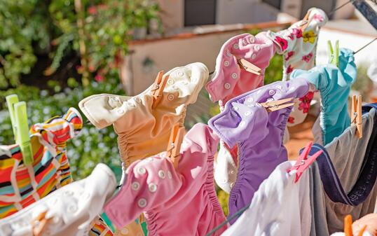 Cloth diapers hanging while drying under the sun on clothesline. Laundry of colorful reusable nappies for babies.