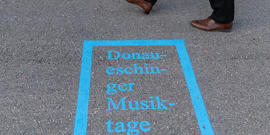 ARCHIV - Ein Mann läuft am Logo der Donaueschinger Musiktage vor der Donauhalle vorbei. Die Donaueschinger Musiktage sind nach Angaben der Veranstalter das weltweit älteste und renommierteste Festival für Neue Musik. Foto: Patrick Seeger/dpa