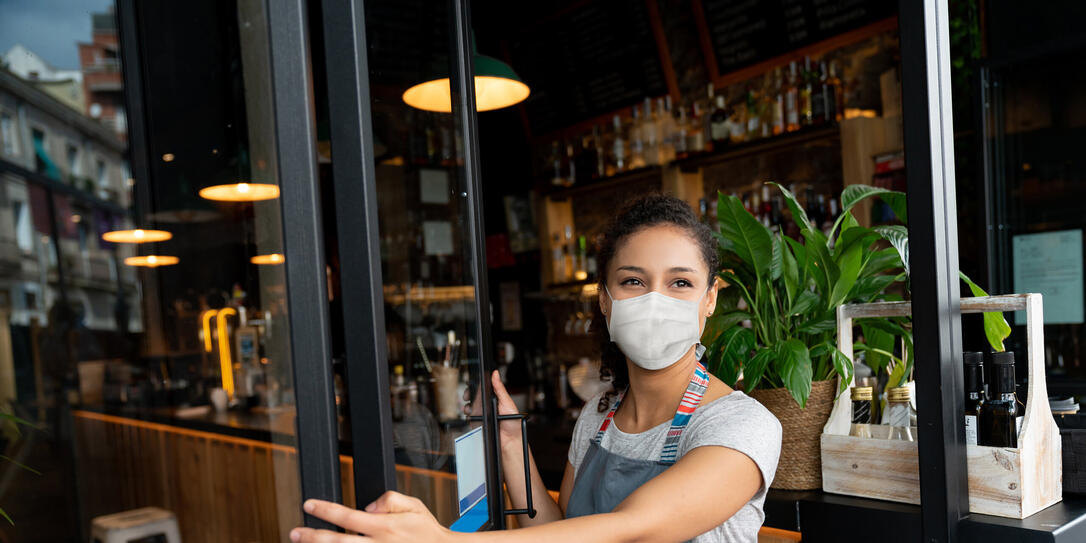 Happy business owner opening the door at a cafe wearing a facemask Happy business owner opening the door at a cafe wearing a facemask