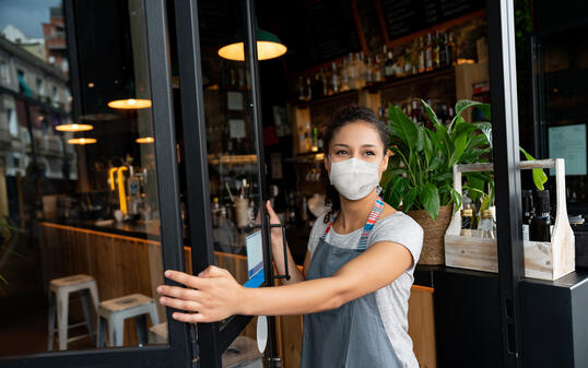 Happy business owner opening the door at a cafe wearing a facemask