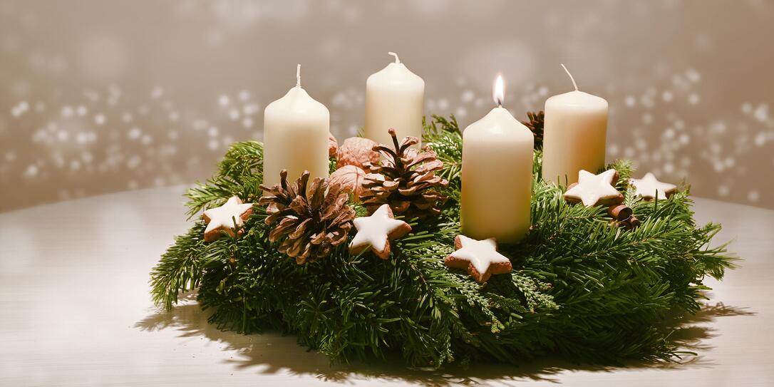 First Advent - decorated Advent wreath from fir and evergreen branches with white burning candles, tradition in the time before Christmas, warm background with festive bokeh and copy space