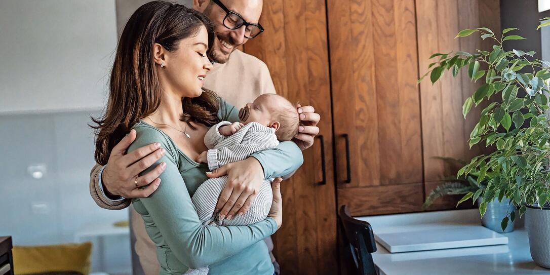 Portrait of young happy man and woman holding newborn cute babe dressed in white unisex clothing.