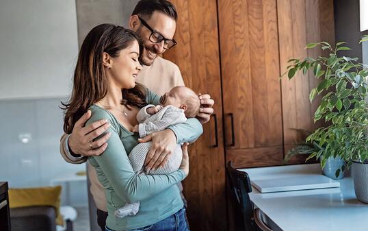 Portrait of young happy man and woman holding newborn cute babe dressed in white unisex clothing.