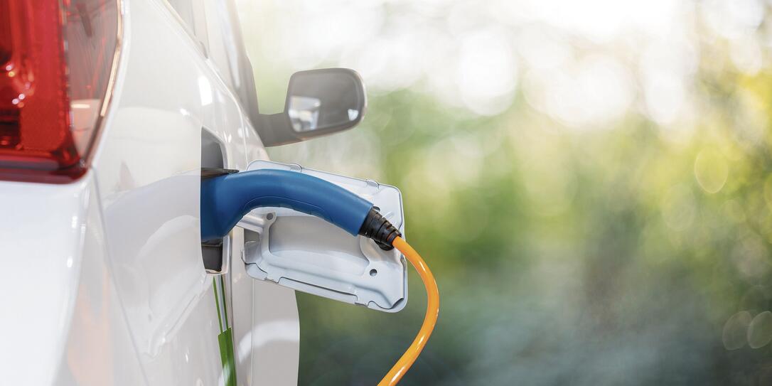 Close up of electric car inlet with a connected charging cable on a green background