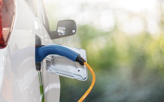 Close up of electric car inlet with a connected charging cable on a green background