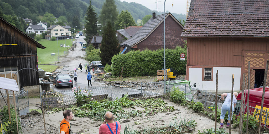 Menschen sind in Kradolf-Schönenberg mit Aufräumarbeiten beschäftigt. Teile des Dorfs waren am Sonntag bei heftigen Gewittern von Bächen überflutet worden. (KEYSTONE/Gian Ehrenzeller)