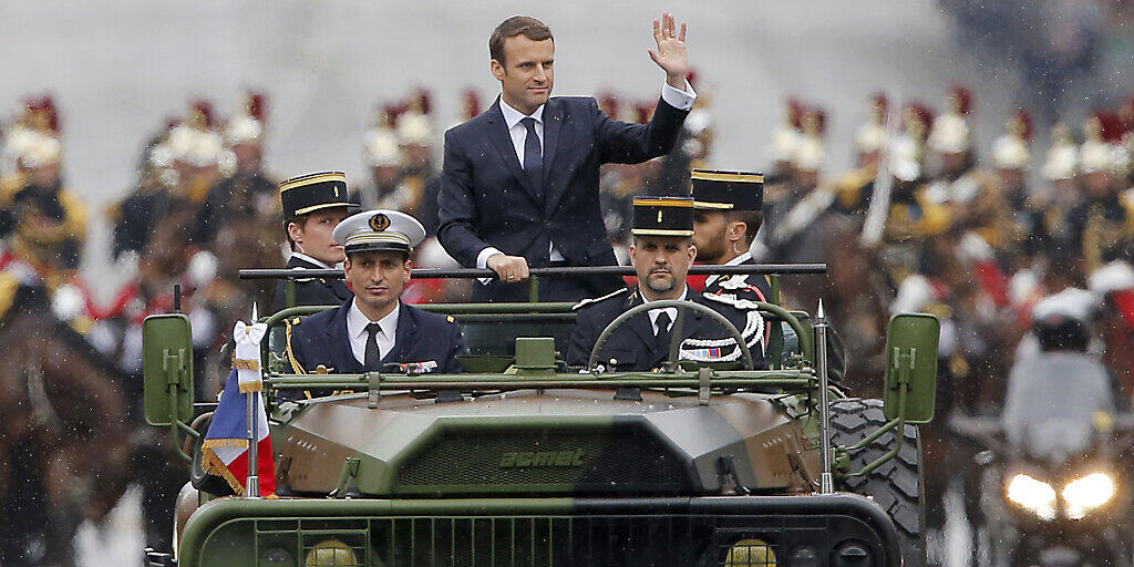 ARCHIV - Der französische Präsident Emmanuel Macron (M) wird in einem Militärfahrzeug bei einer Parade über die Champs-Elysees in Paris gefahren. Frankreich verzichtet wegen der Corona-Krise auf die traditionelle Militärparade am Nationalfeiertag 14. Juli. Foto: Michel Euler/Pool AP/dpa