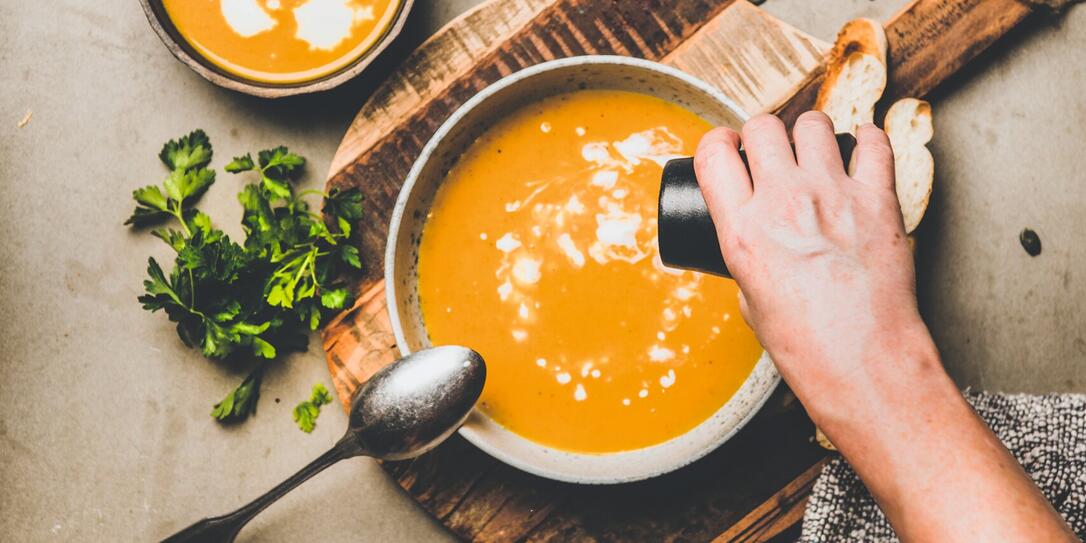 Mans hand adding pepper to pumpkin cream soup with seeds Mans hand adding pepper to pumpkin cream soup with seeds