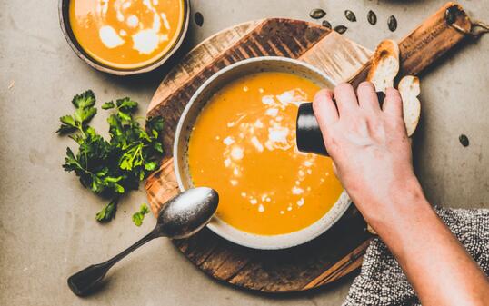 Mans hand adding pepper to pumpkin cream soup with seeds