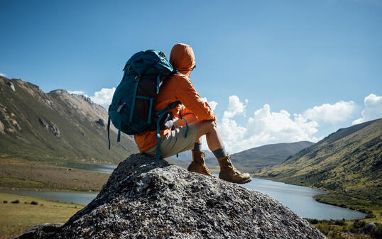 Backpacking woman sit on high altitude mountain top,enjoy the view of a lake in the distance