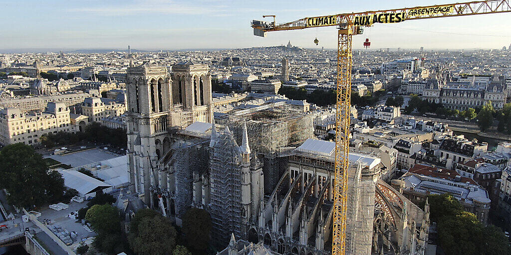 HANDOUT - Ein Transparent: "Klima. In Aktion" ist an einem Kran an der Baustelle der Kathedrale Notre Dame befestigt. Mit einer Aktion auf der Baustelle der Kathedrale Notre-Dame hat die Umweltschutzorganisation Greenpeace in Paris für Aufsehen gesorgt. Foto: Uncredited/Greenpeace/AP/dpa - ACHTUNG: Nur zur redaktionellen Verwendung und nur mit vollständiger Nennung des vorstehenden Credits