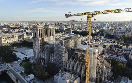 HANDOUT - Ein Transparent: "Klima. In Aktion" ist an einem Kran an der Baustelle der Kathedrale Notre Dame befestigt. Mit einer Aktion auf der Baustelle der Kathedrale Notre-Dame hat die Umweltschutzorganisation Greenpeace in Paris für Aufsehen gesorgt. Foto: Uncredited/Greenpeace/AP/dpa - ACHTUNG: Nur zur redaktionellen Verwendung und nur mit vollständiger Nennung des vorstehenden Credits