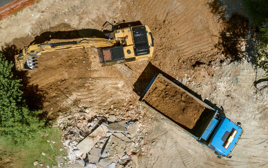 Excavator loading dug out soil onto truck at building site