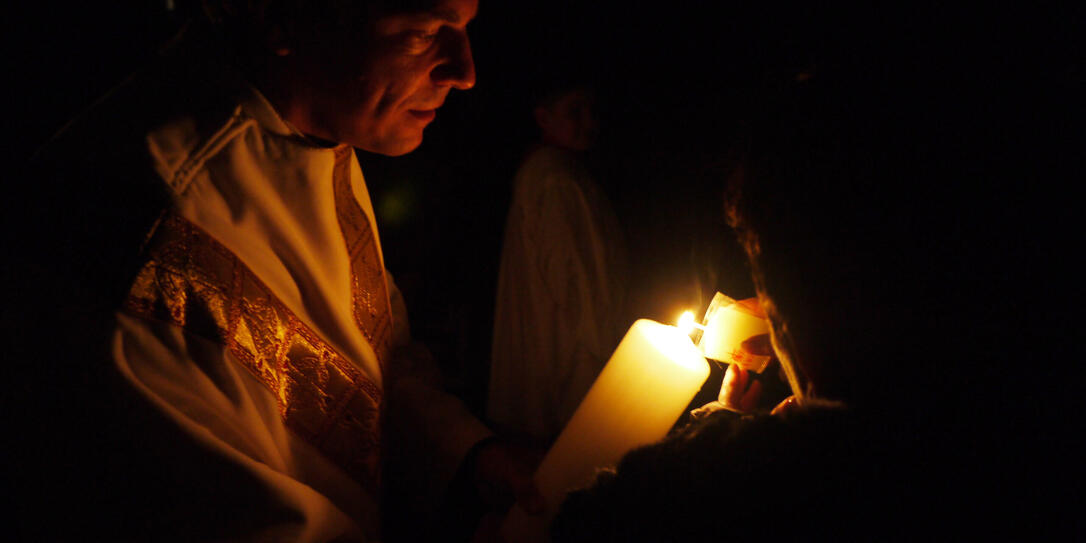 In der noch dunklen Kirche wird das Osterlicht weitergegeben.