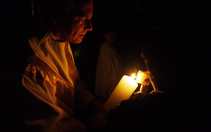 In der noch dunklen Kirche wird das Osterlicht weitergegeben.
