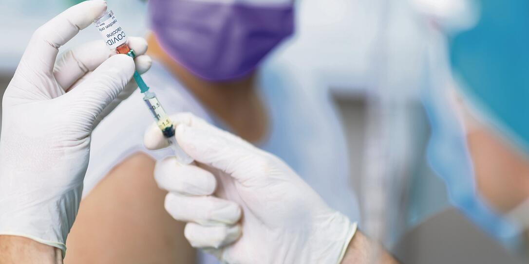 Doctor's hands in surgical gloves preparing COVID-19 vaccine for female patient