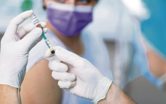 Doctor's hands in surgical gloves preparing COVID-19 vaccine for female patient