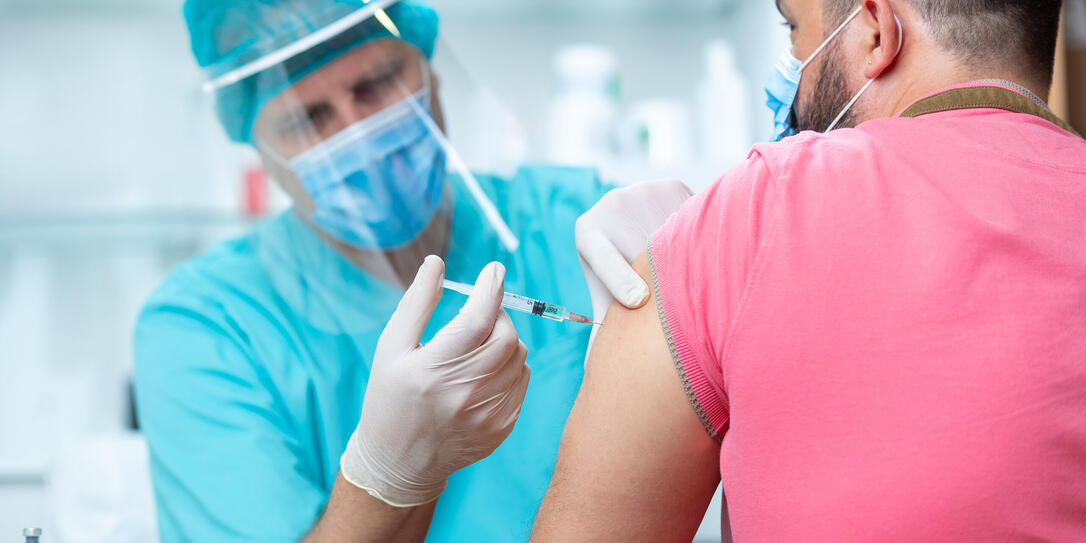 Doctor wearing protective workwear injecting vaccine into patient's arm Doctor wearing protective workwear injecting vaccine into patient's arm