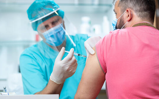 Doctor wearing protective workwear injecting vaccine into patient's arm