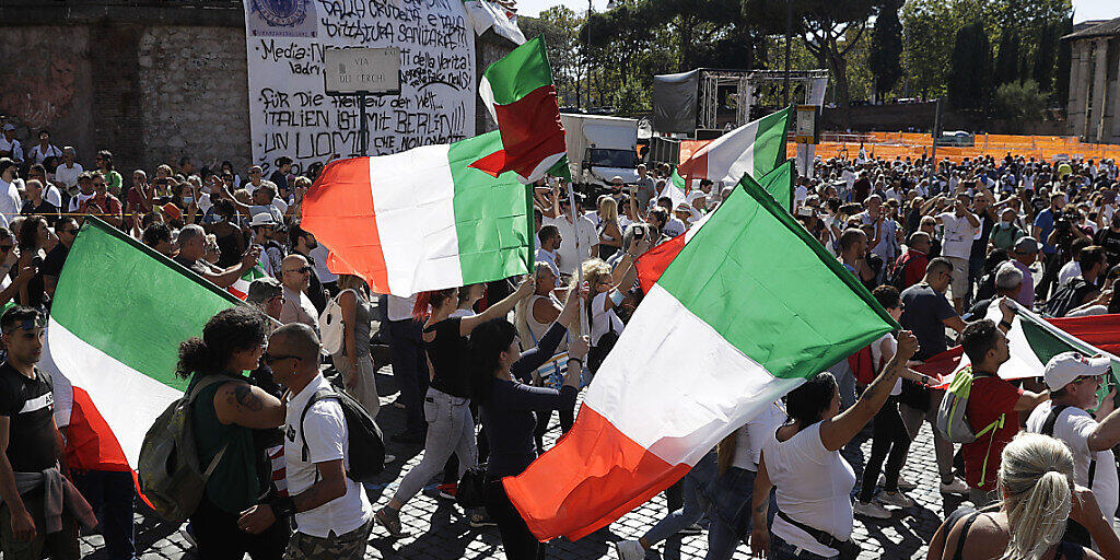 Teilnehmer einer Demonstration gegen die staatliche Corona-Politik schwenken italienische Nationalflaggen. Foto: Gregorio Borgia/AP/dpa
