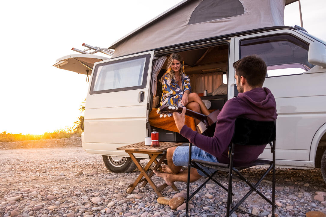 Couple with their camper van on a beach at sunset